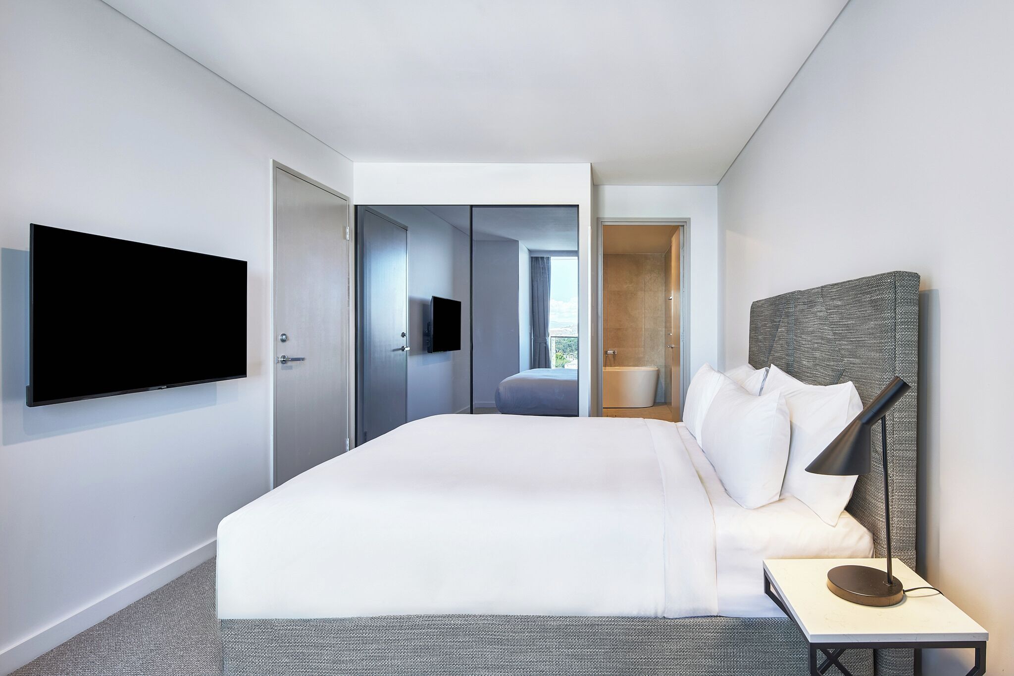 Une chambre d’hôtel moderne dotée d’un grand lit, d’un téléviseur à écran plat fixé au mur et d’une table de chevet avec une lampe.