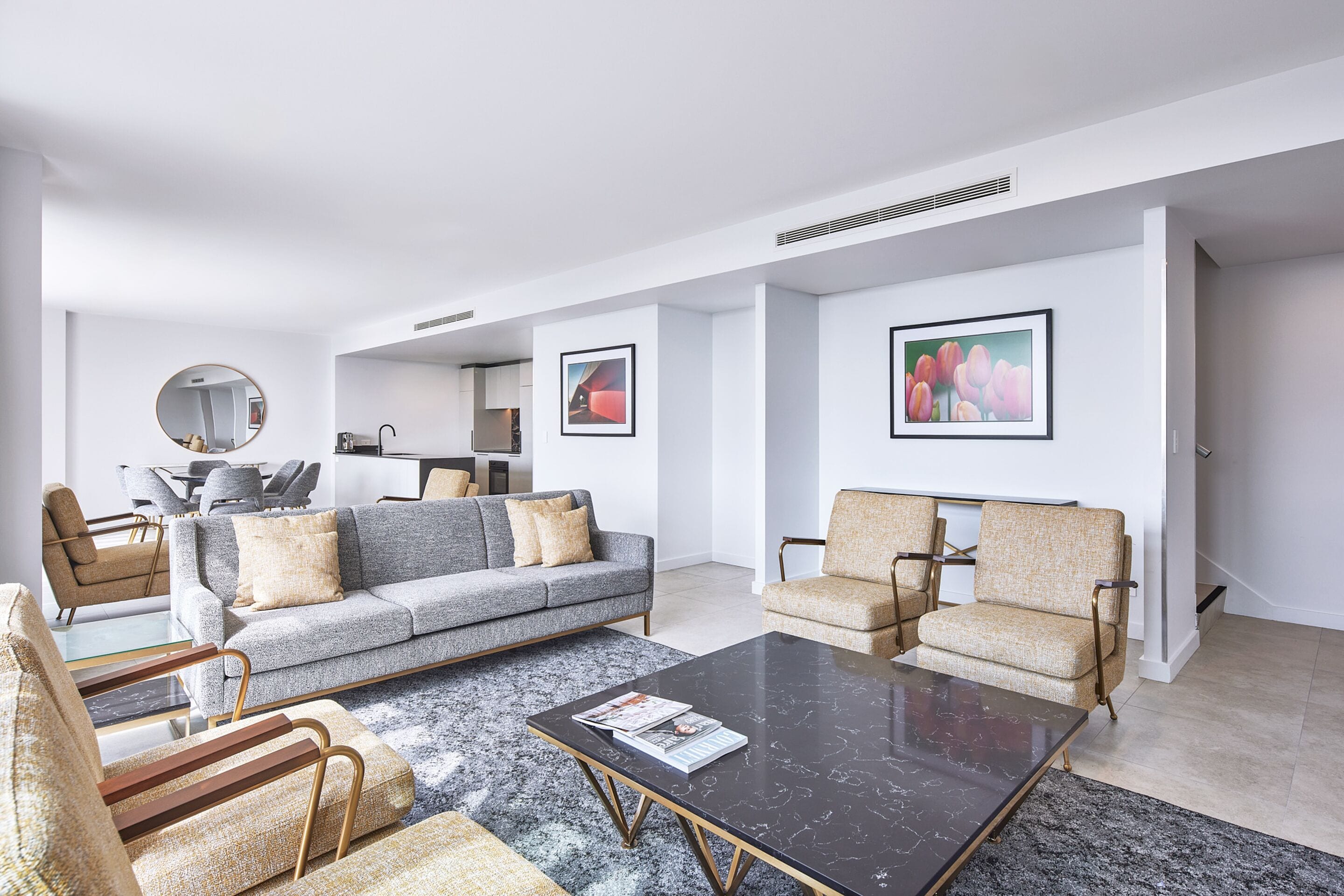 A modern living room with a grey sofa, beige armchairs, a black coffee table, and a large mirror.