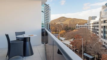 Un balcón con una mesa redonda y sillas, con vistas a un paisaje urbano con edificios modernos y una colina al fondo.