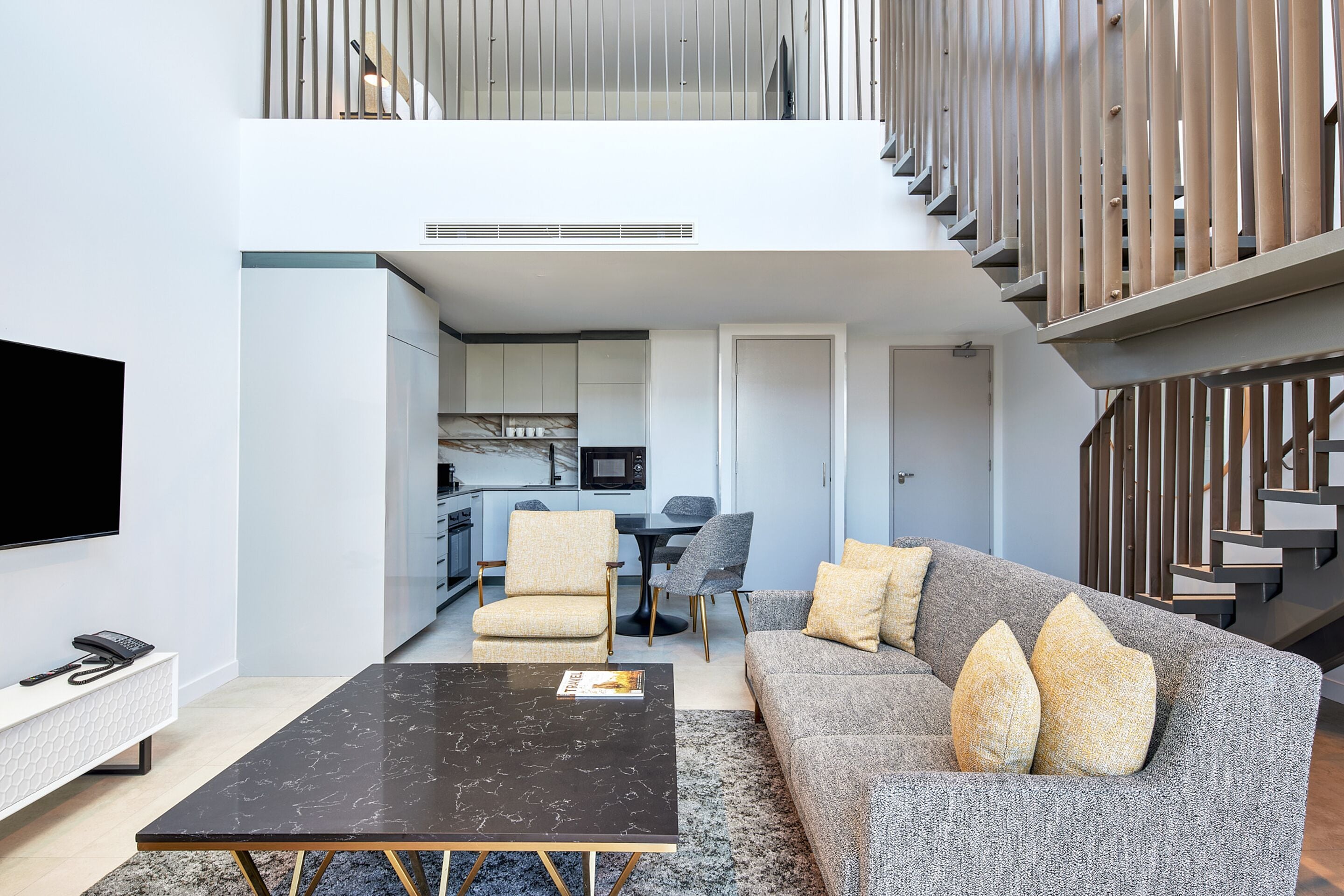 A modern living room with a sofa, coffee table, and TV. There is a staircase leading to an upper level.