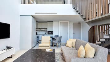 A modern living room with a sofa, coffee table, and TV. There is a staircase leading to an upper level.