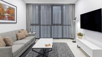 A modern living room with a grey sofa, a white coffee table, a large flat-screen TV, and a grey patterned rug.