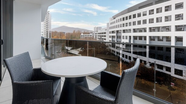 A balcony with a round table and two chairs, overlooking a modern building and a clear sky. - Meriton Suites Canberra (Canberra)