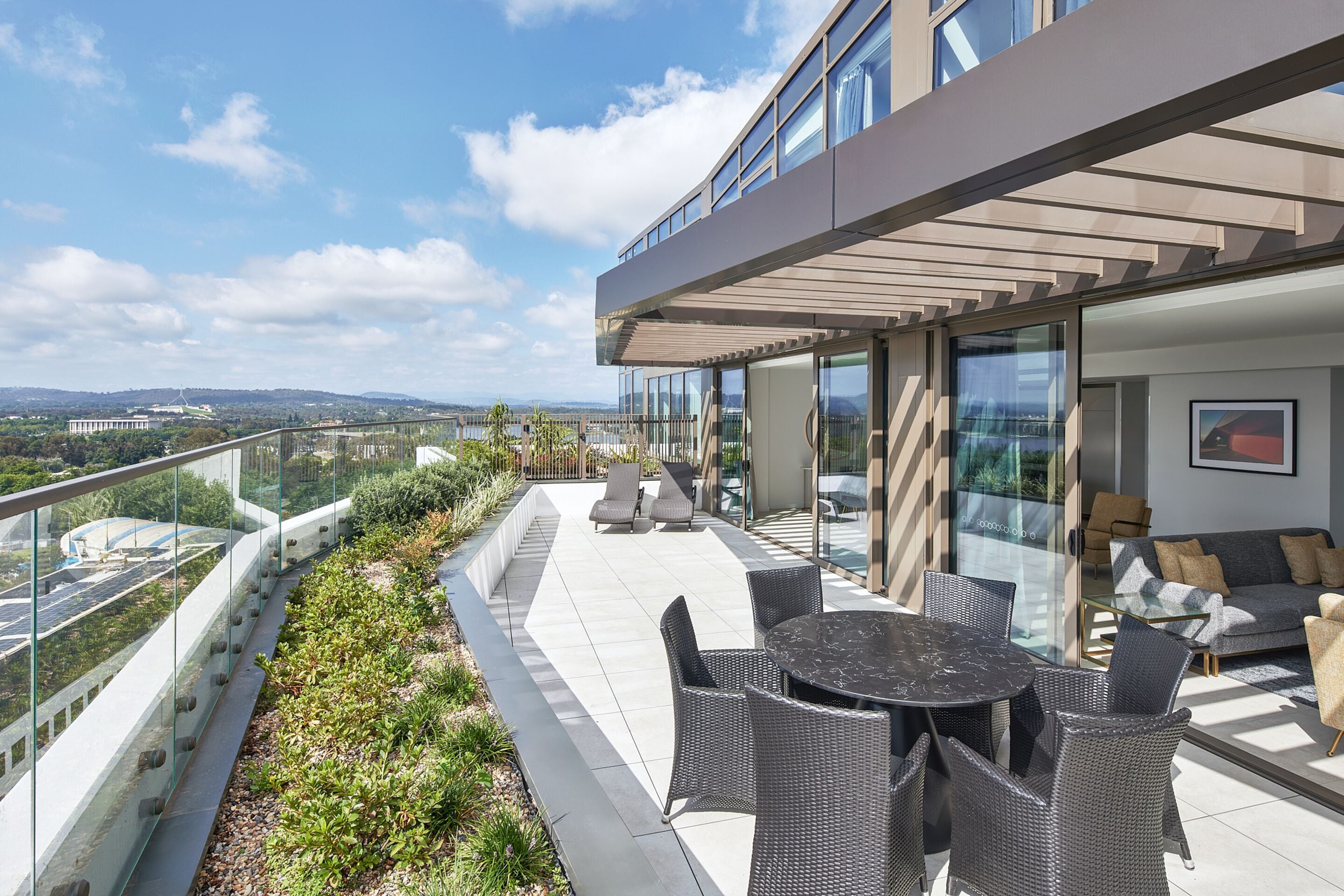 Eine moderne Außenterrasse mit Glasgeländer, Korbmöbeln und Blick auf die Skyline.