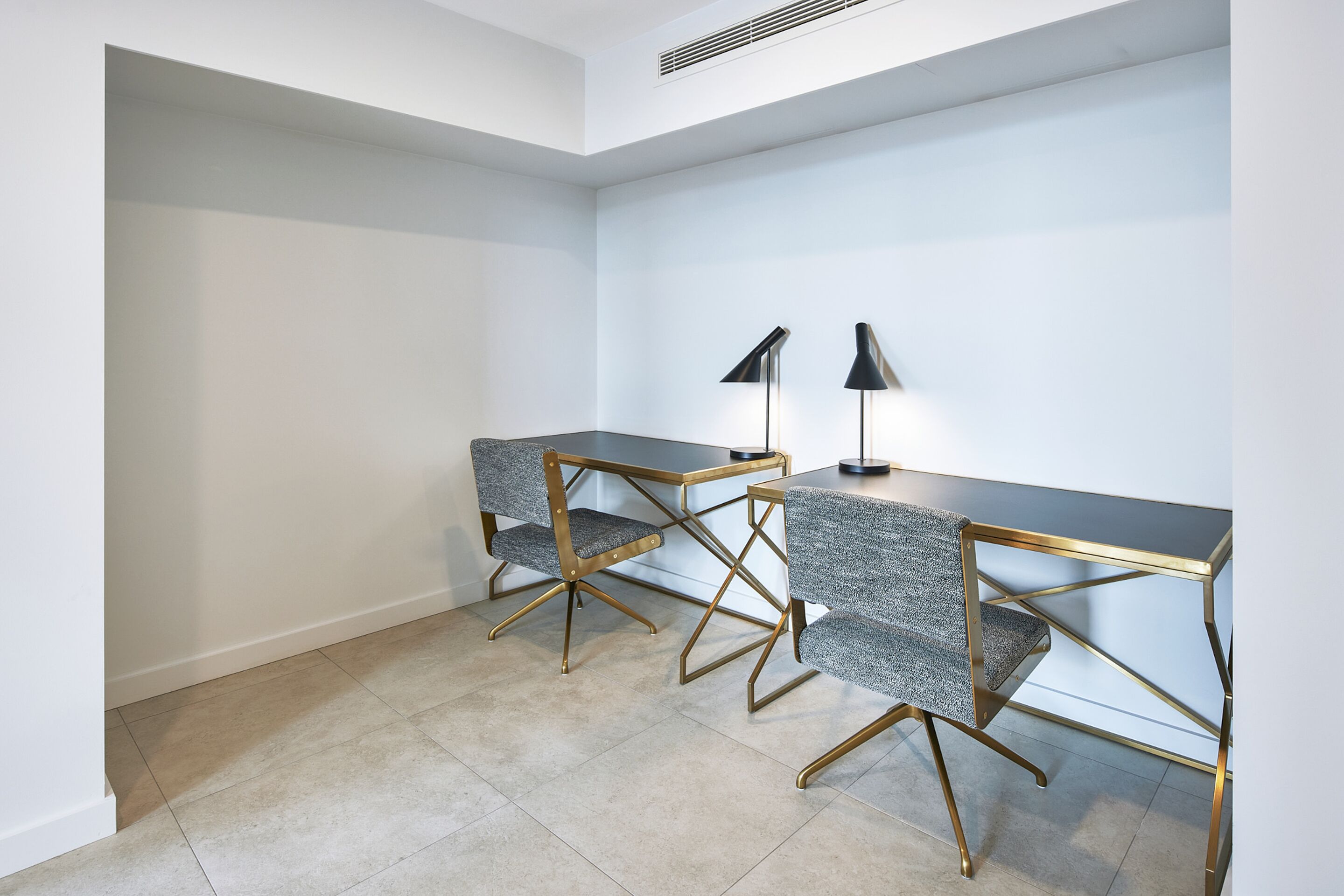 A modern, minimalist office space with two desks and chairs, each with a unique design, and a black desk lamp on one of the desks.
