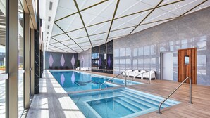 Una piscina interior con un diseño moderno, que incluye un techo geométrico y suelo de madera.