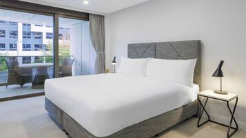 A modern hotel room with a large bed, a small bedside table with a lamp, and a view of the outside balcony.