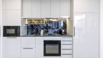 A modern kitchen with white cabinetry, a black oven, and a marble backsplash.