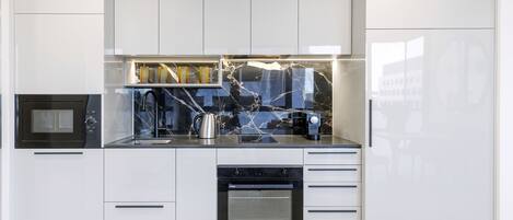 Une cuisine moderne avec des meubles blancs, un four noir et un pare-feu en marbre.