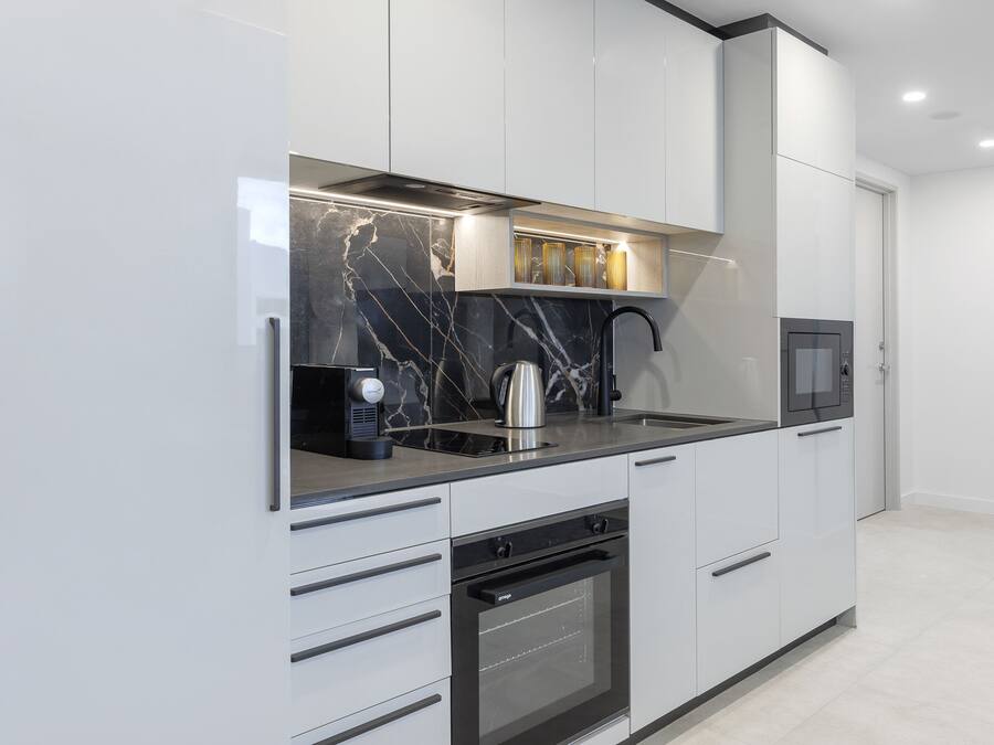Een moderne keuken met witte kasten, een zwart aanrecht, een ingebouwde oven en een magnetron.
