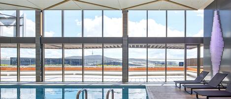 A modern indoor swimming pool with clear views of the cityscape through large windows.