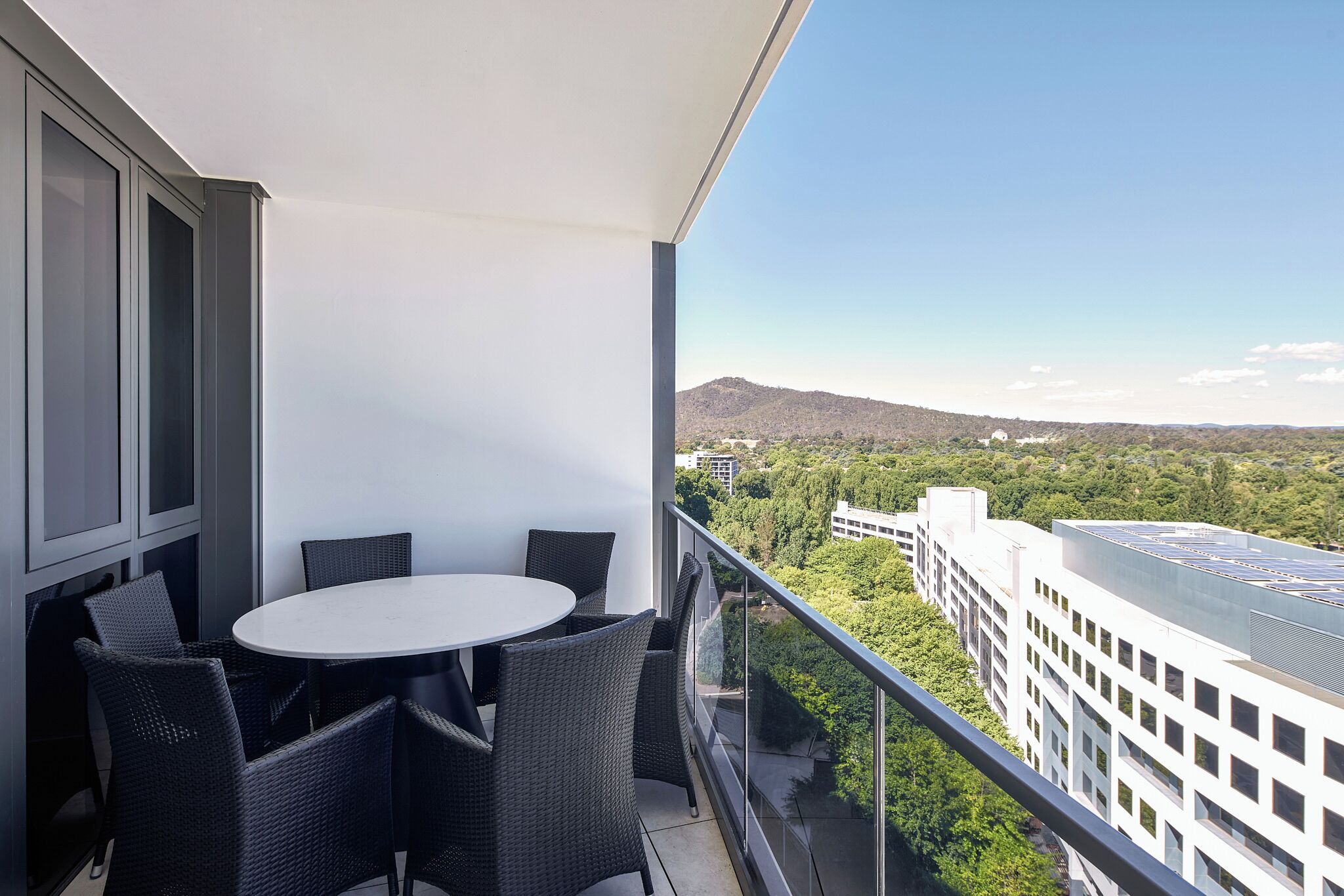 A balcony with a round table and chairs, overlooking a cityscape with buildings and greenery.