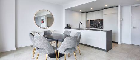 A modern kitchen with white cabinets, a marble backsplash, and a round mirror above the dining table.