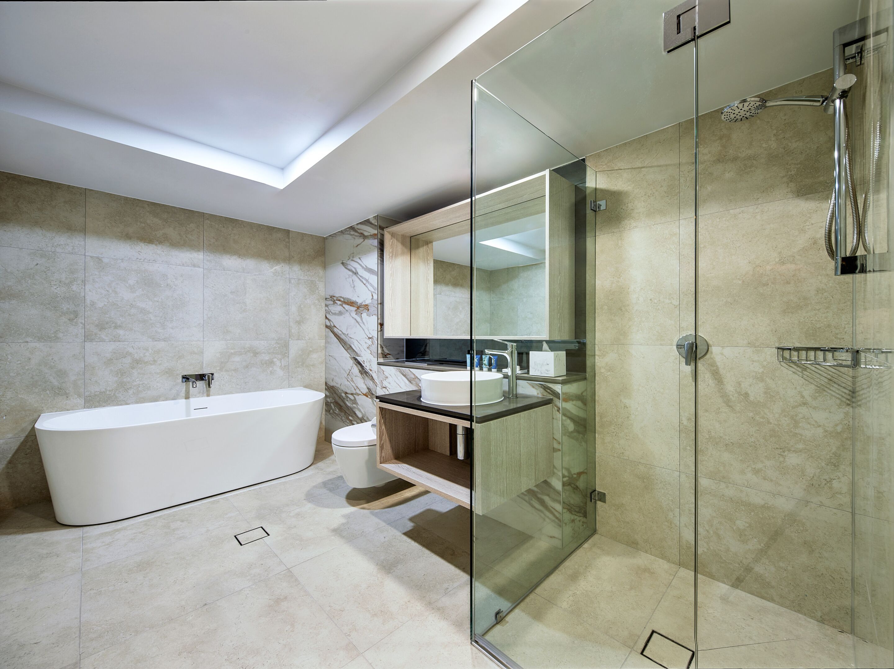 Een moderne badkamer met een vrijstaand bad, een douche met glazen wanden en een wand betegeld met marmer.