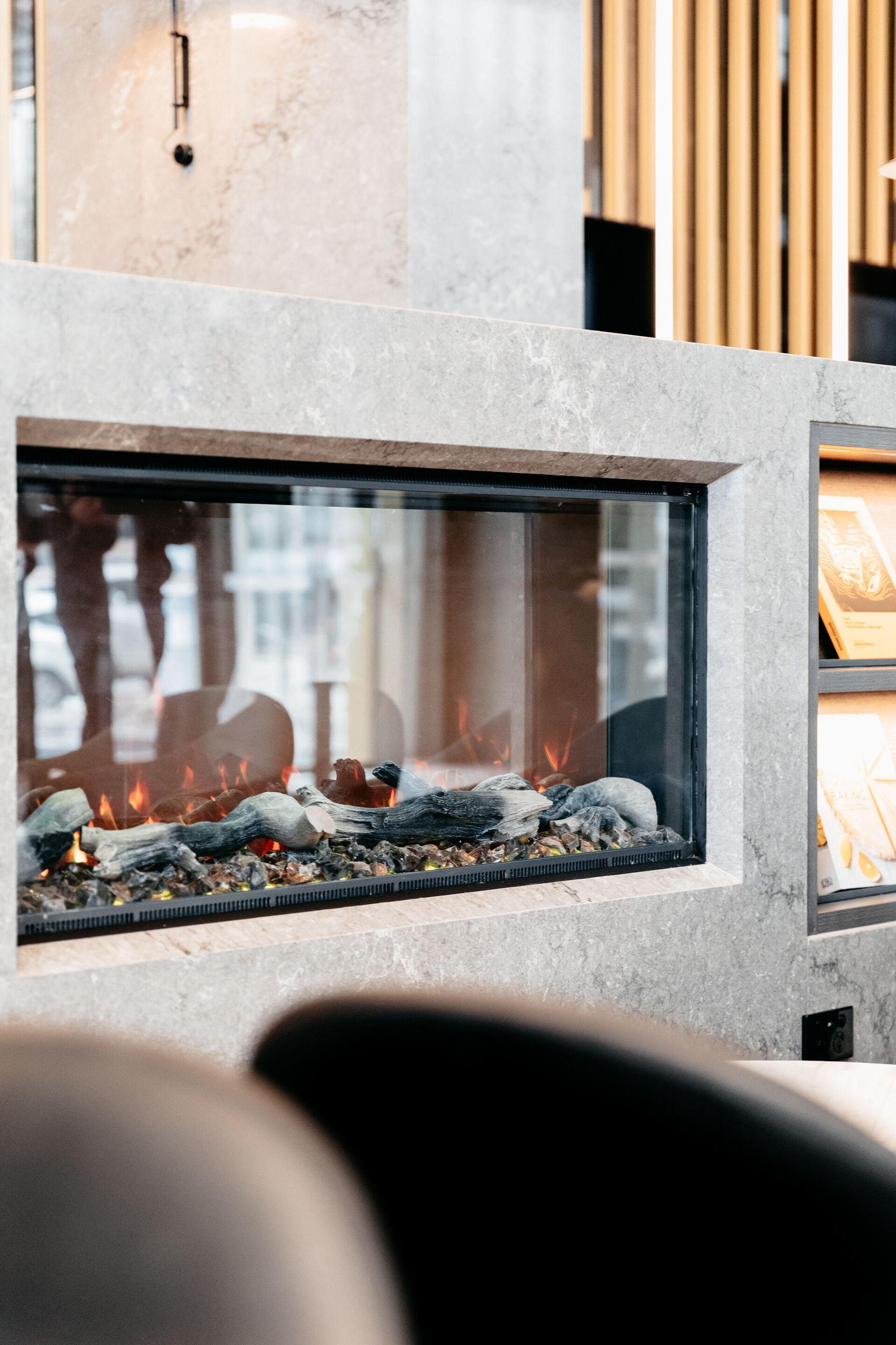 Une cheminée moderne avec une façade en verre, des bûches et des braises incandescentes.