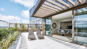 Un patio moderno al aire libre con sillones de descanso, un comedor y una cocina con paredes de vidrio.