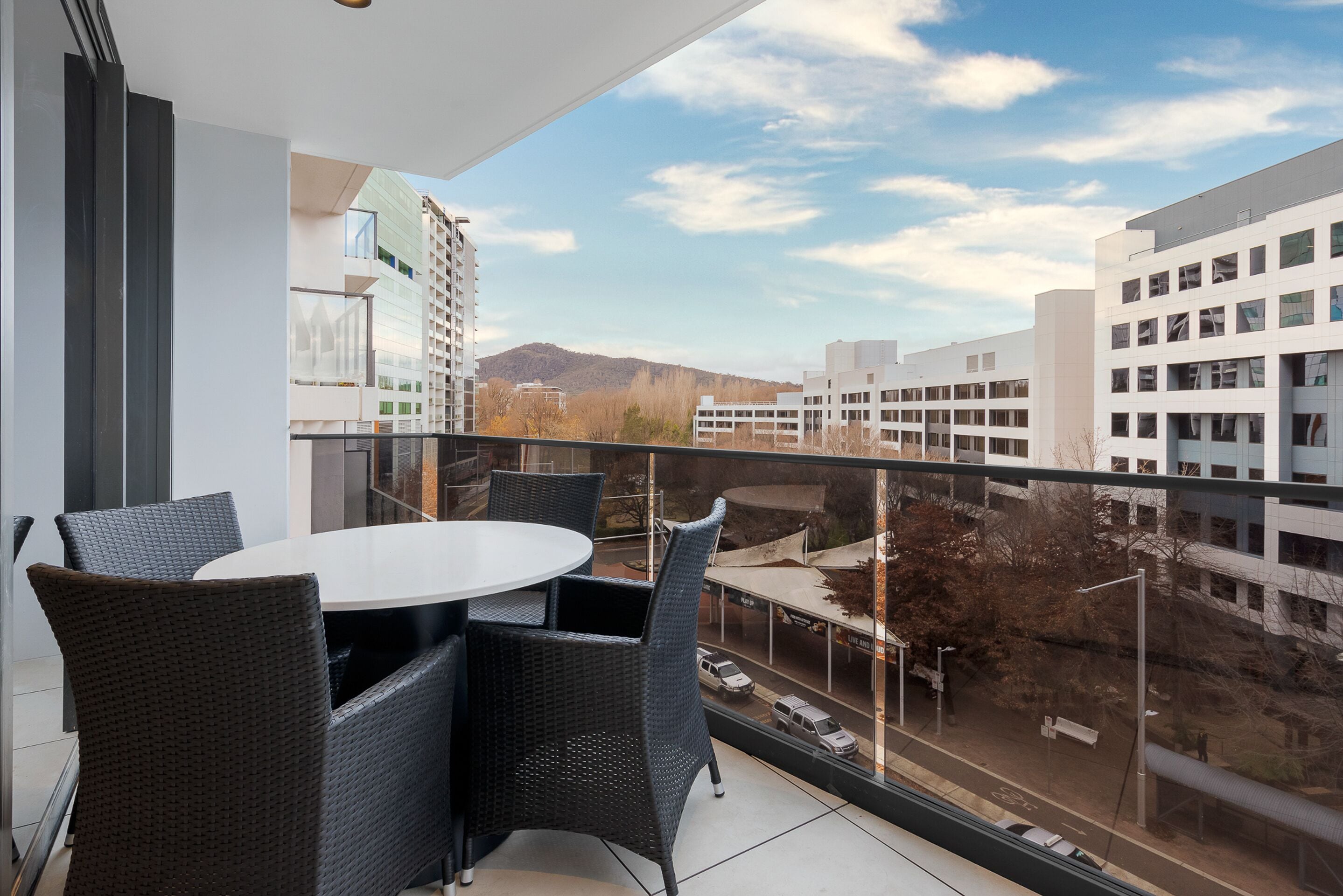 Een balkon met een ronde tafel en stoelen, met uitzicht op een stadsgezicht met gebouwen en een verafgelegen berg.