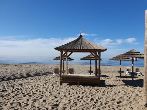 A beach with a wooden gazebo, beach chairs, and thatched umbrellas.