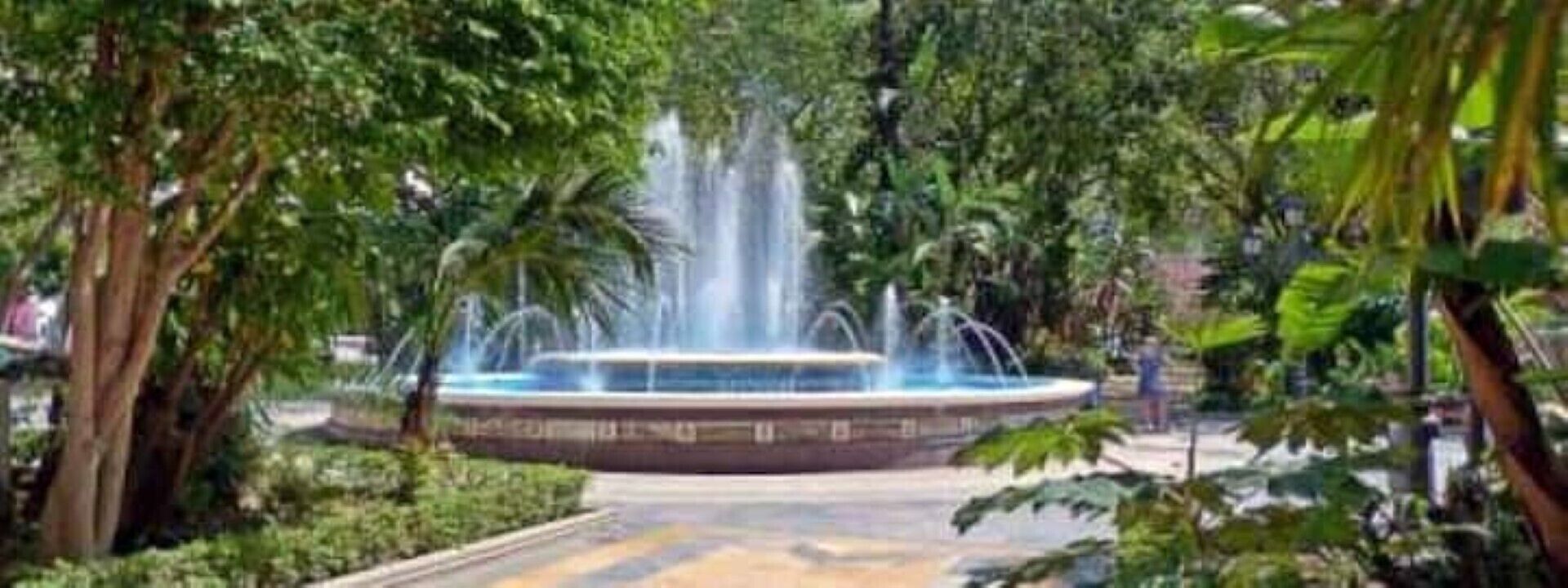 Ein kreisrunder Brunnen, umgeben von üppigem Grün in einer Parkanlage.