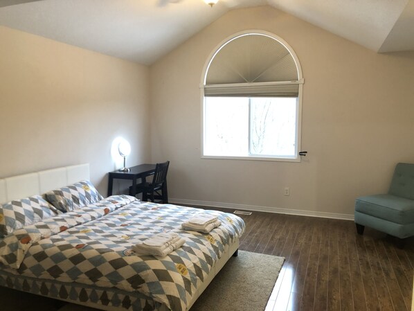 A bedroom with a bed, a desk, a chair, a window, and a small sofa.