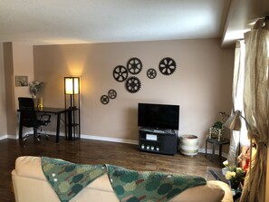 A living room with a sofa, a TV, a coffee table, a lamp, and wall decorations.