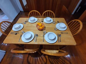 Mesa de madeira posta com pratos brancos, talheres e uma cesta de laranjas.