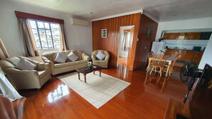 A living room with a sofa, armchairs, a coffee table, and a dining area with wooden chairs and a table.