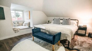 A bedroom with a bed, a bench, a nightstand, a lamp, and a window with a view.