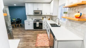 A modern kitchen with white cabinets, a microwave, a stove, and a sink. There is a dining area with a table and chairs, and a rug on the floor.