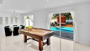 A pool table in a modern room with a view of a swimming pool and outdoor seating.