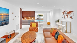 A modern living room with a sofa, a coffee table, and a dining area with a white table and chairs.