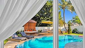 A pool area with lounge chairs, a sun umbrella, and a wooden structure.