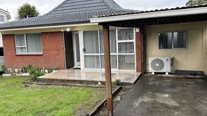 A residential house with a tiled roof, a covered patio, and a large air conditioning unit. - Cheerful 3 bedroom  with free parking (Auckland)