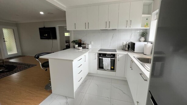 A modern kitchen with white cabinets, a built-in oven, and a refrigerator. - Cheerful 3 bedroom  with free parking (Auckland)