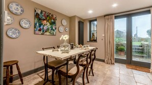 Comedor con una mesa preparada para cuatro personas, rodeada de sillas. En la pared, un cuadro abstracto de gran tamaño, una ventana con cortinas y vistas al exterior.