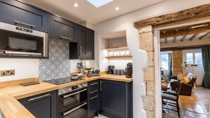 Cocina moderna con armarios oscuros, microondas y horno empotrado. Se aprecia una pared de piedra y una viga de techo de madera.