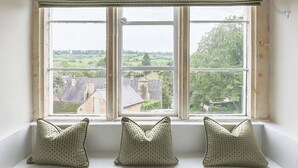 Ventana con tres almohadones en un alféizar, con vista a un paisaje rural.