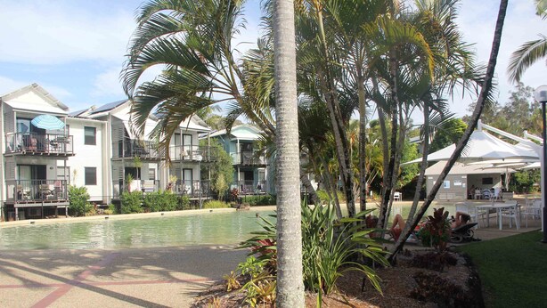 Um resort com piscina, palmeiras e áreas de estar ao ar livre.