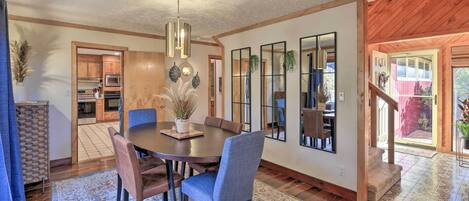 A dining area with a round table, chairs, and a rug. There is a kitchen visible through an open doorway.