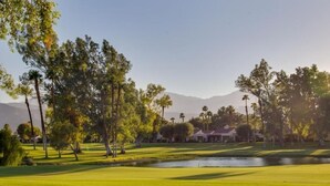 Un parcours de golf avec un étang, des arbres et des maisons en arrière-plan.