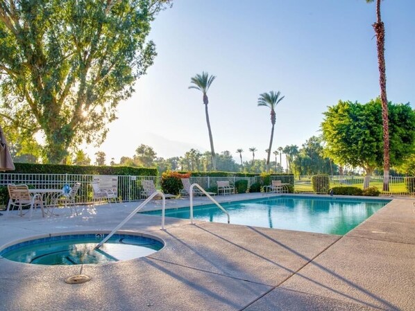A swimming pool with a hot tub, surrounded by lounge chairs and palm trees.