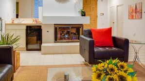 Un salon moderne avec une cheminée, un canapé agrémenté d’un coussin rouge et une table basse en verre.