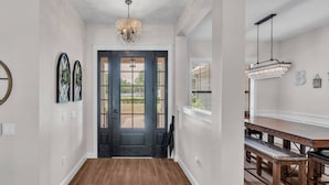 A hallway with a wooden floor, a black door, and a chandelier.
