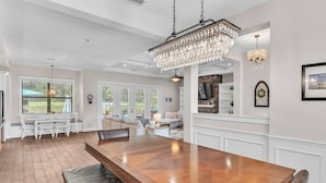 A spacious dining area with a large wooden table, white walls, and a chandelier.