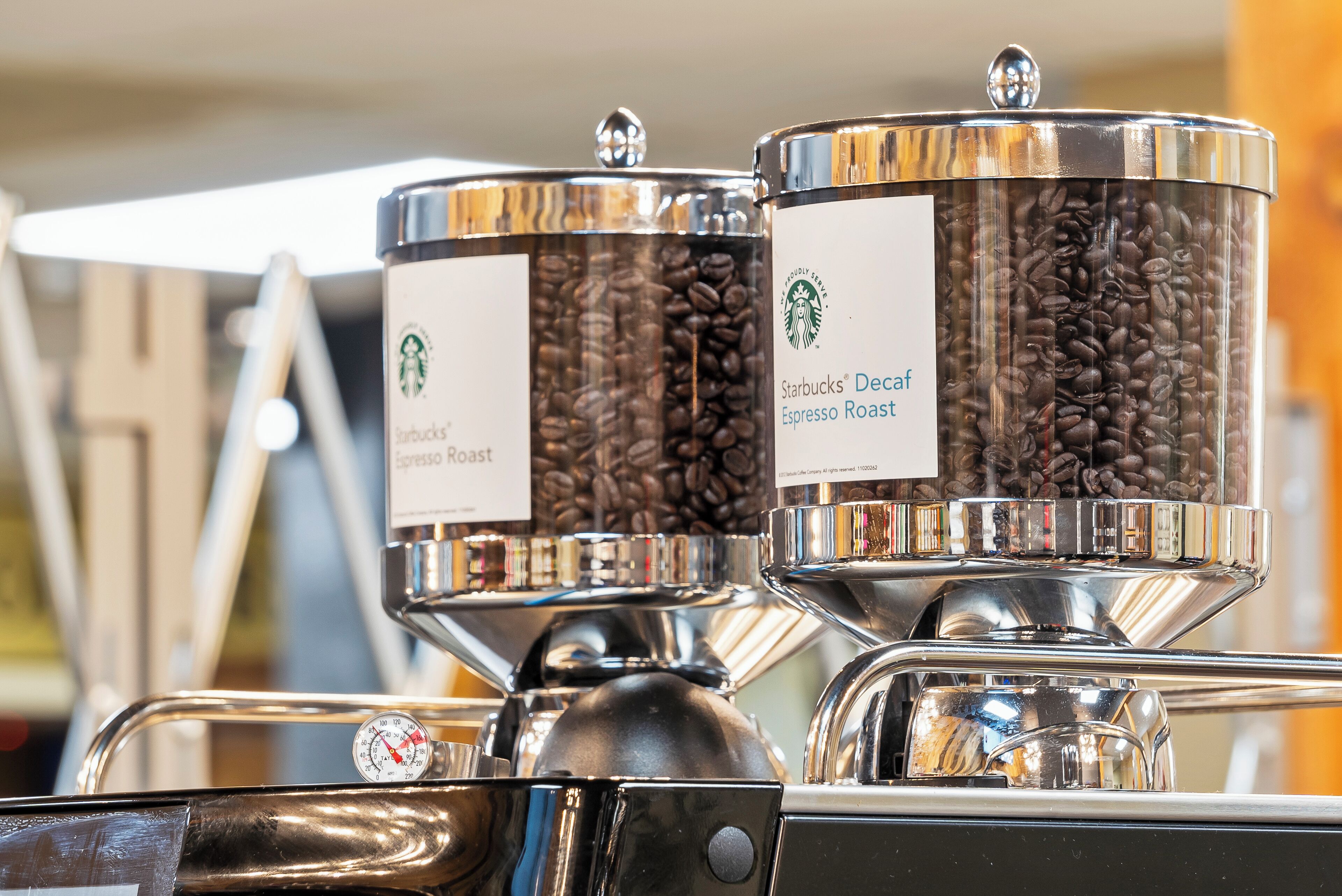 Two coffee dispensers labeled 'Starbucks Decaf Espresso Roast' and 'Espresso Roast' with a coffee bean hopper and a pressure gauge.