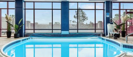 Une piscine intérieure à l’eau d’un bleu cristallin, entourée de grandes fenêtres qui offrent une vue sur l’extérieur.