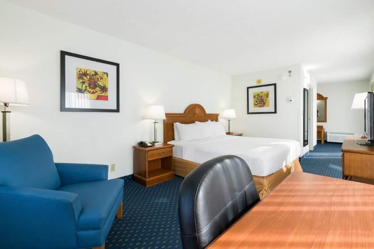 Quarto de hotel com cama, escrivaninha, cadeira, sofá e duas mesas de cabeceira com abajures.