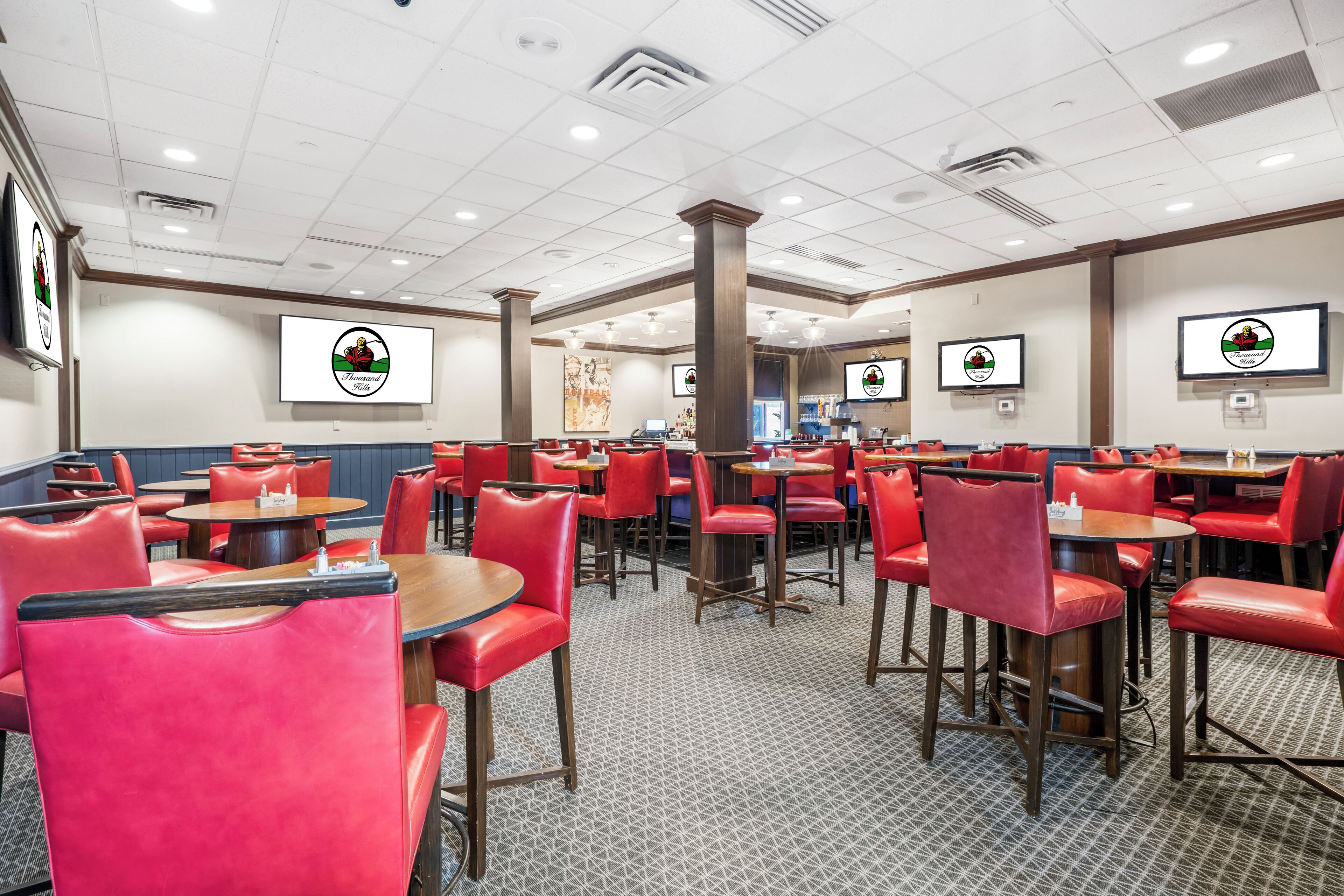 A restaurant with red chairs and tables, a patterned floor, and screens displaying the restaurant's logo.