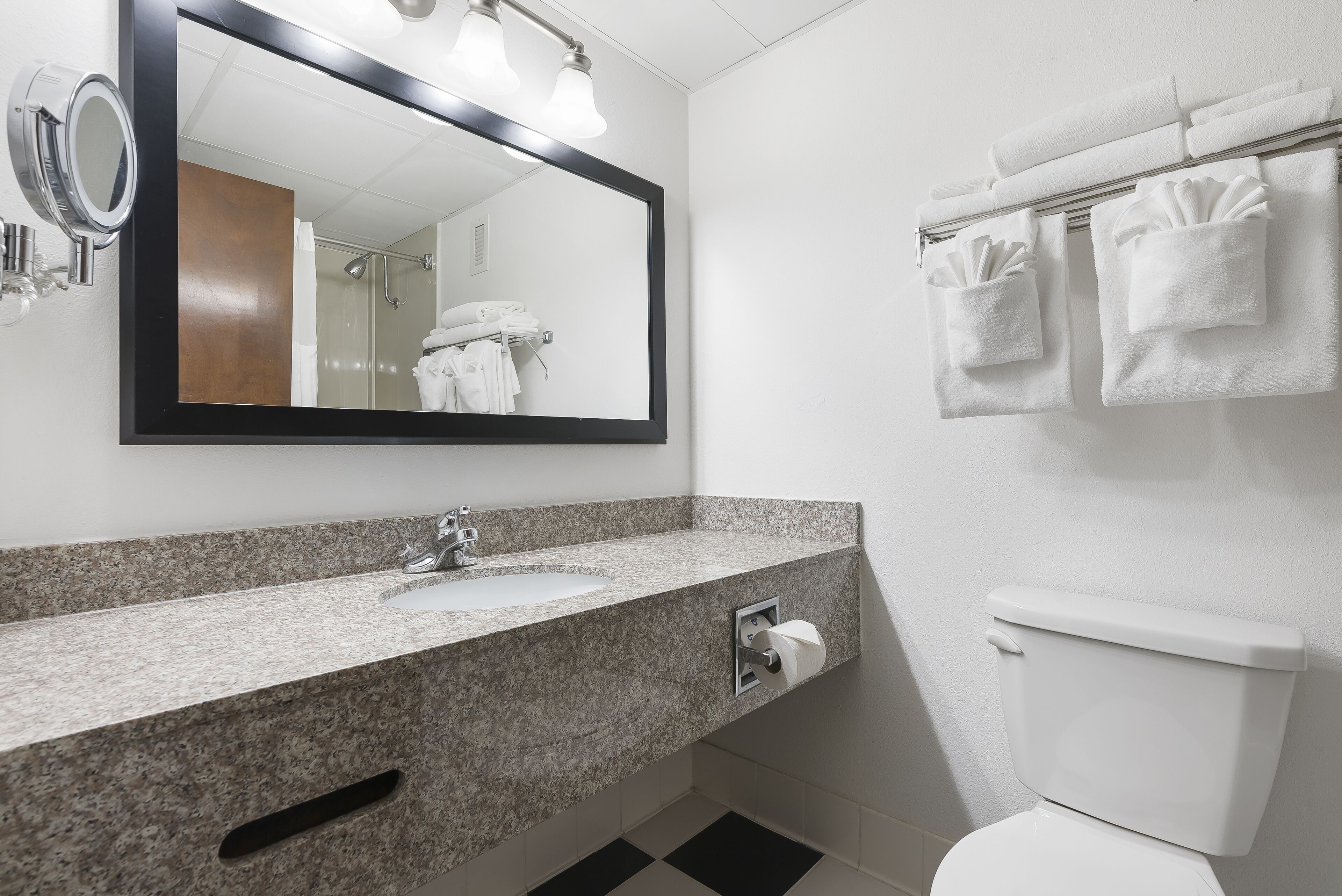 Baño con lavamanos de encimera de granito, un espejo, toallero con toallas blancas y un inodoro.