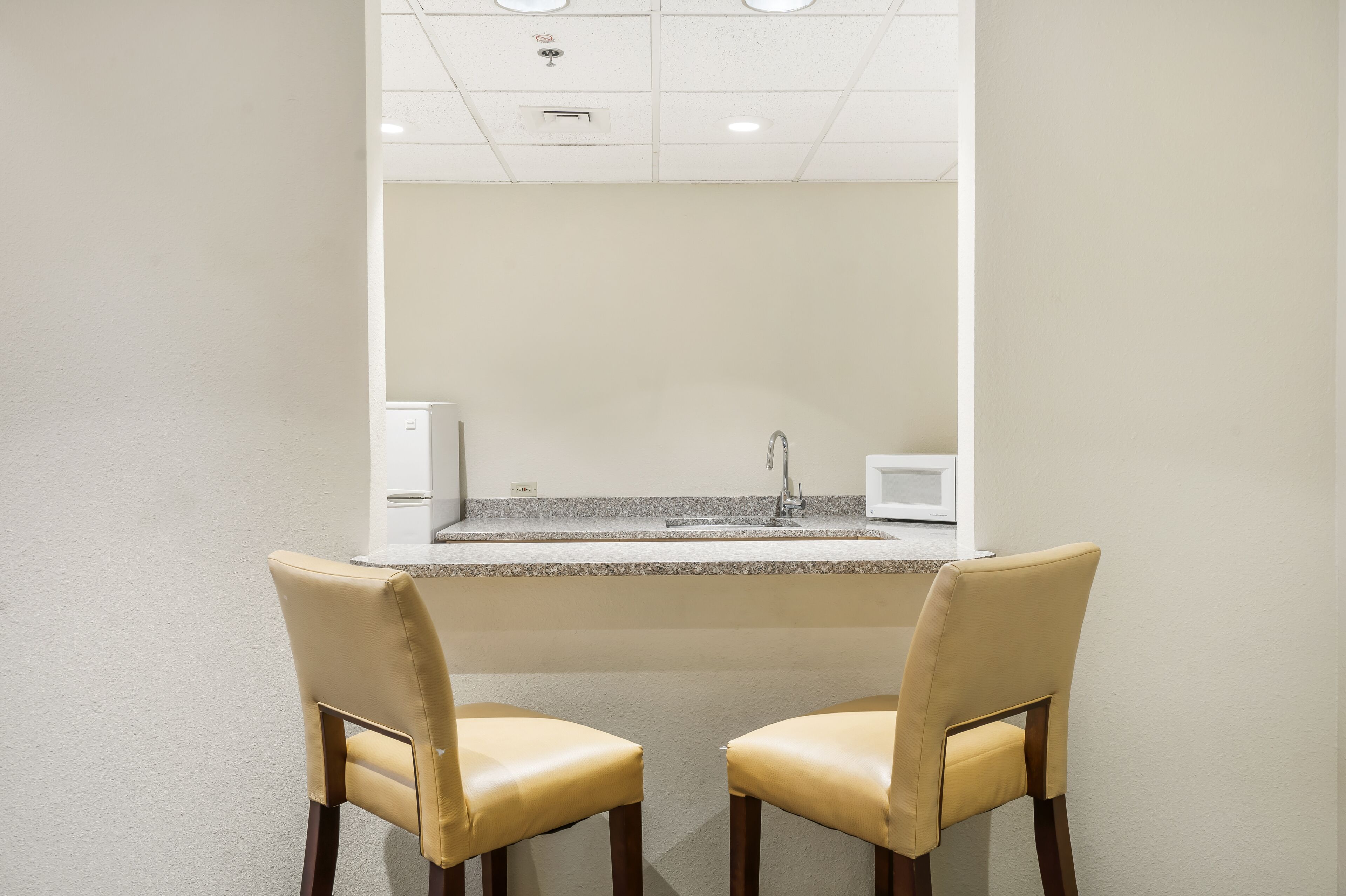 A bathroom with a sink, mirror, and two chairs.